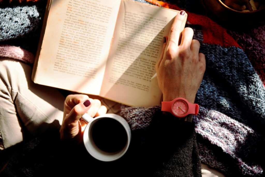 Person reading a book while holding a cup of coffee, capturing the relaxed focus of being absorbed in page turner books